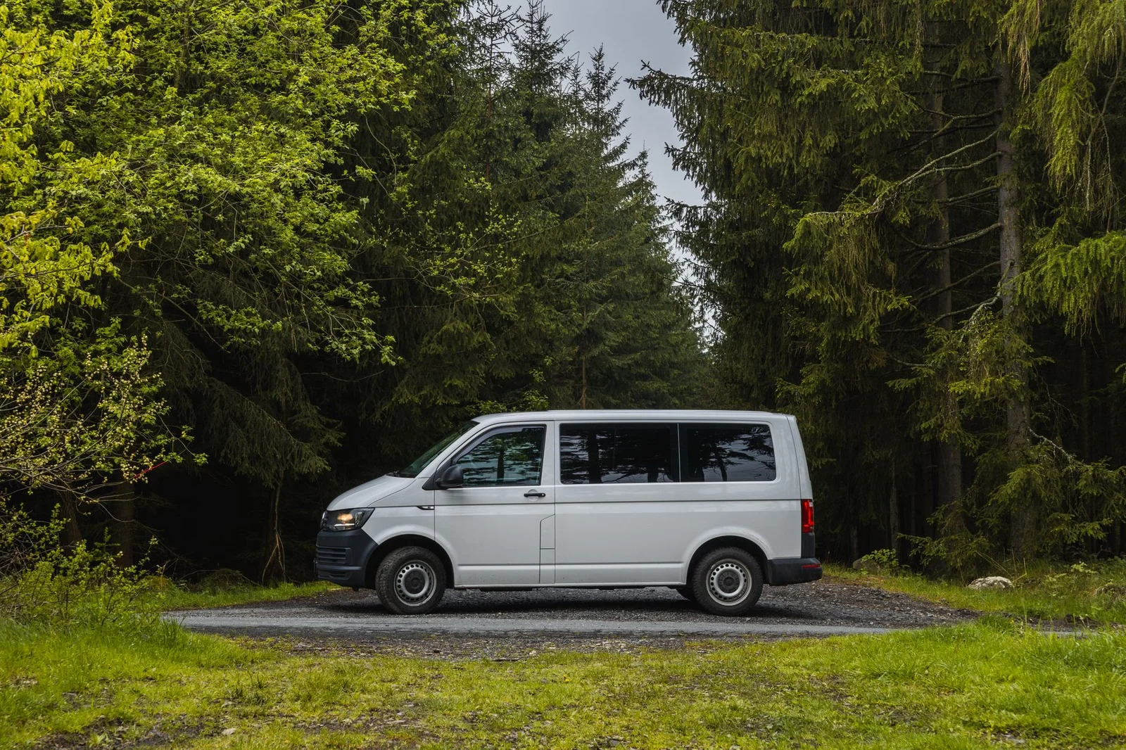Weißer VW Transporter in Seitenansicht auf einem Waldweg als Symbolbild für den Camper-Umbau eines VW T6