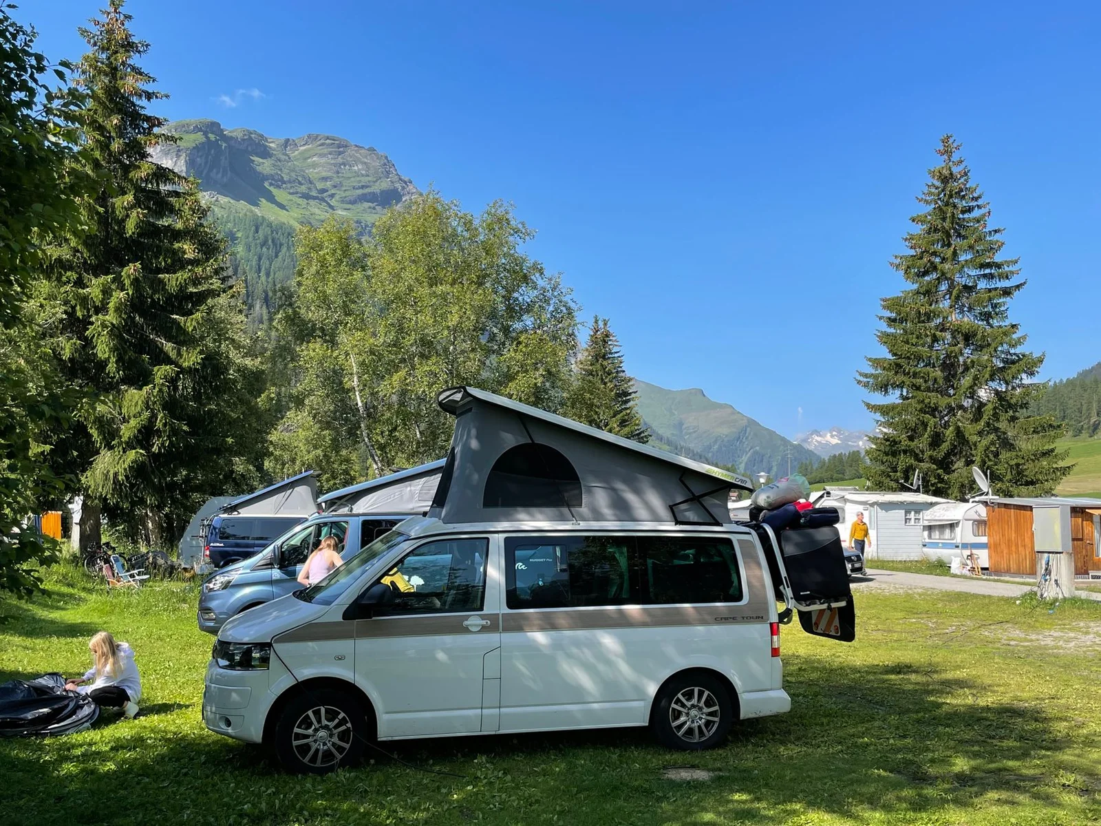 VW Camper mit aufgestelltem Hochdach auf sonnigem Bergcampingplatz
