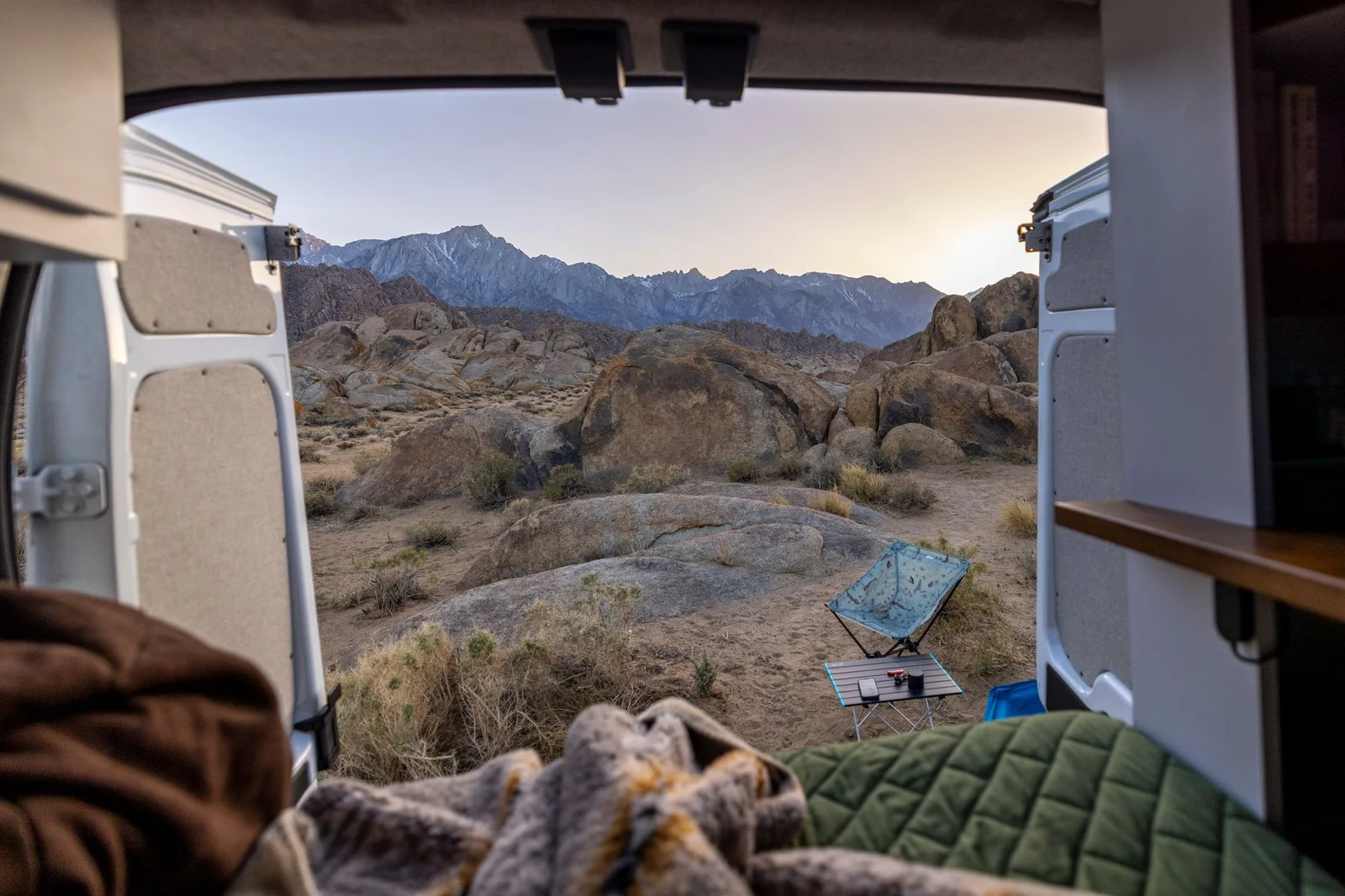 Blick aus einem Campingfahrzeug auf eine helle Berglandschaft mit Campingstuhl